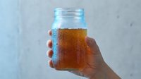 Hand holding glass jar filled with cold cola or iced tea beverage with condensation droplets, isolated on white background for beverage packaging and advertising use.