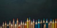 Colorful wooden pencils arranged in row against dark green chalkboard background, creating artistic composition for education and creativity concepts.