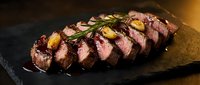 Sliced grilled beef steak with rosemary garnish on dark slate plate. Premium meat cooked medium rare with herbs for gourmet dining and culinary presentations.