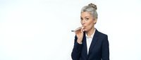Senior woman with gray hair wearing dark blazer and white shirt, holding pen thoughtfully near mouth, isolated on white background for business and professional concepts.