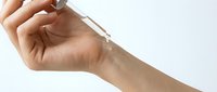 Caucasian woman applying clear serum with dropper on wrist, skincare routine concept on light background, beauty and wellness treatment.