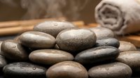 Smooth river stones with water droplets arranged for spa treatment with bamboo and towel creating zen wellness atmosphere for relaxation therapy.