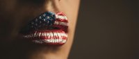 Woman lips painted with American flag stars and stripes pattern for patriotic makeup concept on dark background.