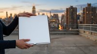 Businessman holding blank white tablet with urban skyline at sunset, ideal for corporate messaging and advertising campaigns on rooftop.