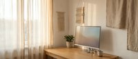 Modern minimalist home office workspace with computer monitor on wooden desk near window with natural light and neutral decor for productivity and focus.