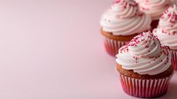 Chocolate cupcakes with swirled vanilla buttercream frosting topped with red sprinkles on pink background. Selective focus creates dreamy Valentine's Day mood.