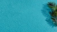 Aerial view of crystal clear turquoise ocean water surface with gentle ripples and palm tree shadow in corner, creating minimalist tropical summer scene.