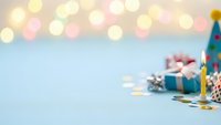Birthday party celebration background with colorful bokeh lights, wrapped gifts, candles and festive decorations on pastel blue surface for greeting cards.