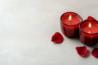Two red candles in glass holders with rose petals on a light background, creating a romantic Valentine's Day or anniversary atmosphere.