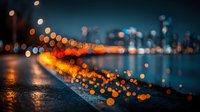 Urban night scene with blurred city lights creating golden bokeh effects along waterfront promenade, atmospheric evening cityscape with warm illumination.