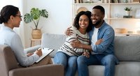 Happy African American couple embracing on couch during therapy session with female counselor in modern office for relationship counseling and support.