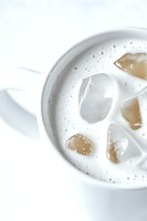 White ceramic cup filled with creamy drink and ice cubes, top view close-up on bright background. Minimalist beverage photography for menu and cafe promotion.