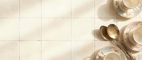 Elegant beige ceramic tiles with warm neutral tones creating sophisticated kitchen or bathroom flooring, complemented by golden tableware and wooden spoons.