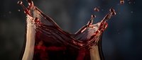Dynamic red wine splash with elegant droplets and fluid motion against dark background for beverage advertising and culinary design projects.