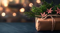 Eco-friendly Christmas gift wrapped in kraft paper with pine branches and pink paper flowers, decorated with twine on dark background with bokeh lights.
