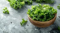 Fresh green curly lettuce leaves in wooden bowl on gray concrete background, healthy organic salad ingredients for cooking and food styling.