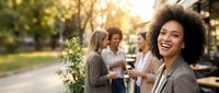 Young African American businesswoman smiling at camera during outdoor team meeting with diverse colleagues in sunny park setting for corporate events.