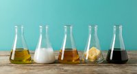 Laboratory glassware with various colored liquids on wooden surface against turquoise background for scientific research and chemistry experiments.