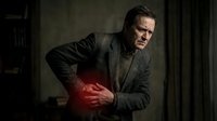 Middle-aged Caucasian businessman in dark suit experiencing severe abdominal pain in dimly lit office environment for medical and healthcare concepts.