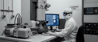 Laboratory technician in protective suit operating advanced scientific equipment with computer monitor in sterile research facility environment.