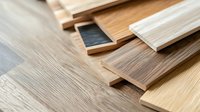 Assorted wood flooring samples in various finishes and tones arranged in overlapping rows, showcasing laminate and vinyl options for home renovation and interior design projects.