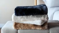 Soft plush blankets stacked in neutral colors of black, gray, white and brown. Cozy fleece throws with faux fur texture for home decor and comfort.