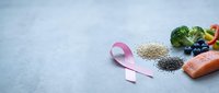 Pink ribbon with healthy foods including salmon, broccoli, blueberries and quinoa on gray background for cancer awareness and prevention nutrition.