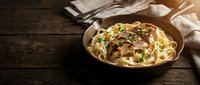 Creamy pasta with mushrooms and herbs served in rustic bowl on wooden table. Comfort food for restaurant menus and culinary blogs.