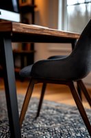 Modern black dining chair with wooden legs against industrial style table, set on ornate blue rug in contemporary home interior with natural lighting.