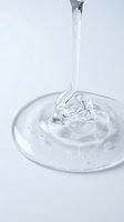 Clear liquid pouring into shallow dish creating dynamic splash and ripple effect. Suitable for skincare, cosmetics, beauty product packaging, and wellness advertising campaigns.