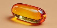 Transparent amber capsule with golden liquid inside on beige background, casting warm shadow, used in pharmaceutical or supplement advertising.