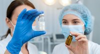 Two female medical professionals in surgical masks and caps examining laboratory samples in sterile clinical environment for pharmaceutical research and testing.
