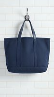 Navy blue canvas tote bag hanging on chrome hook against white subway tile wall background for fashion and lifestyle concepts.