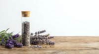 Glass bottle with cork filled with dried lavender seeds on rustic wooden table with fresh purple lavender sprigs for aromatherapy and natural wellness.