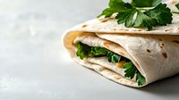 Fresh tortilla wrap filled with green herbs and vegetables on light background, close up view with selective focus and copy space for menu design.