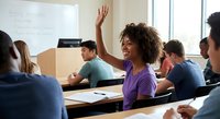 Young African American woman raising hand in university classroom during lecture with diverse students learning together.