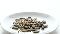Mixed seeds and grains collection on white plate featuring pumpkin seeds, quinoa, chia seeds for healthy cooking and nutrition concepts.