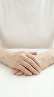 Elderly hands folded together on white surface showing wrinkles and age spots in soft natural lighting for healthcare and aging concepts.