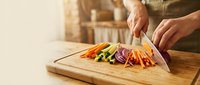 Hands of adult male chef slicing colorful fresh vegetables on wooden cutting board in kitchen, food preparation for cooking and meal planning.