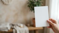 Woman holding blank white card in modern home interior with natural light and green plant decor for mockup and branding purposes.