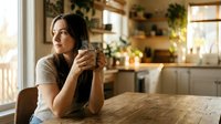 Young woman enjoying morning coffee in bright modern kitchen with wooden countertops and natural lighting creating peaceful domestic atmosphere.