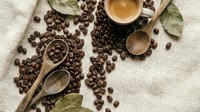 Fresh roasted coffee beans with wooden spoons and cup on rustic burlap background for cafe menu design and culinary projects.