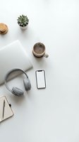 Minimalist flat lay workspace with smartphone blank screen, headphones, laptop, coffee cup, notebook, and succulent on white desk.