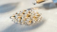 Scattered golden and clear gemstones on white fabric surface with natural sunlight casting shadows, suitable for luxury jewelry, fashion, and design projects.