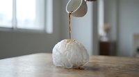 Pouring hot water over white gauze ball for tea brewing, herbal infusion preparation, and wellness beverage making.