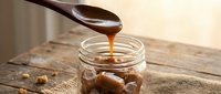 Creamy caramel sauce dripping from wooden spoon into glass jar on rustic table. Sweet dessert topping for ice cream, cakes and pastries.