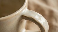 Close-up of handcrafted ceramic pottery handle with smooth beige glaze finish, showcasing artisan craftsmanship and organic curved form against soft background.