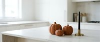 Autumn pumpkins on white marble kitchen counter with brass candlestick, minimalist fall home decor in bright modern interior space.