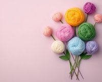 Colorful yarn balls arranged as flowers with green leaves on pink background, creative crafting concept for knitting and crochet projects. Soft pastel colors.