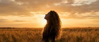 Young woman with long curly hair standing in golden wheat field at sunset, peaceful moment of freedom and connection with nature during golden hour.